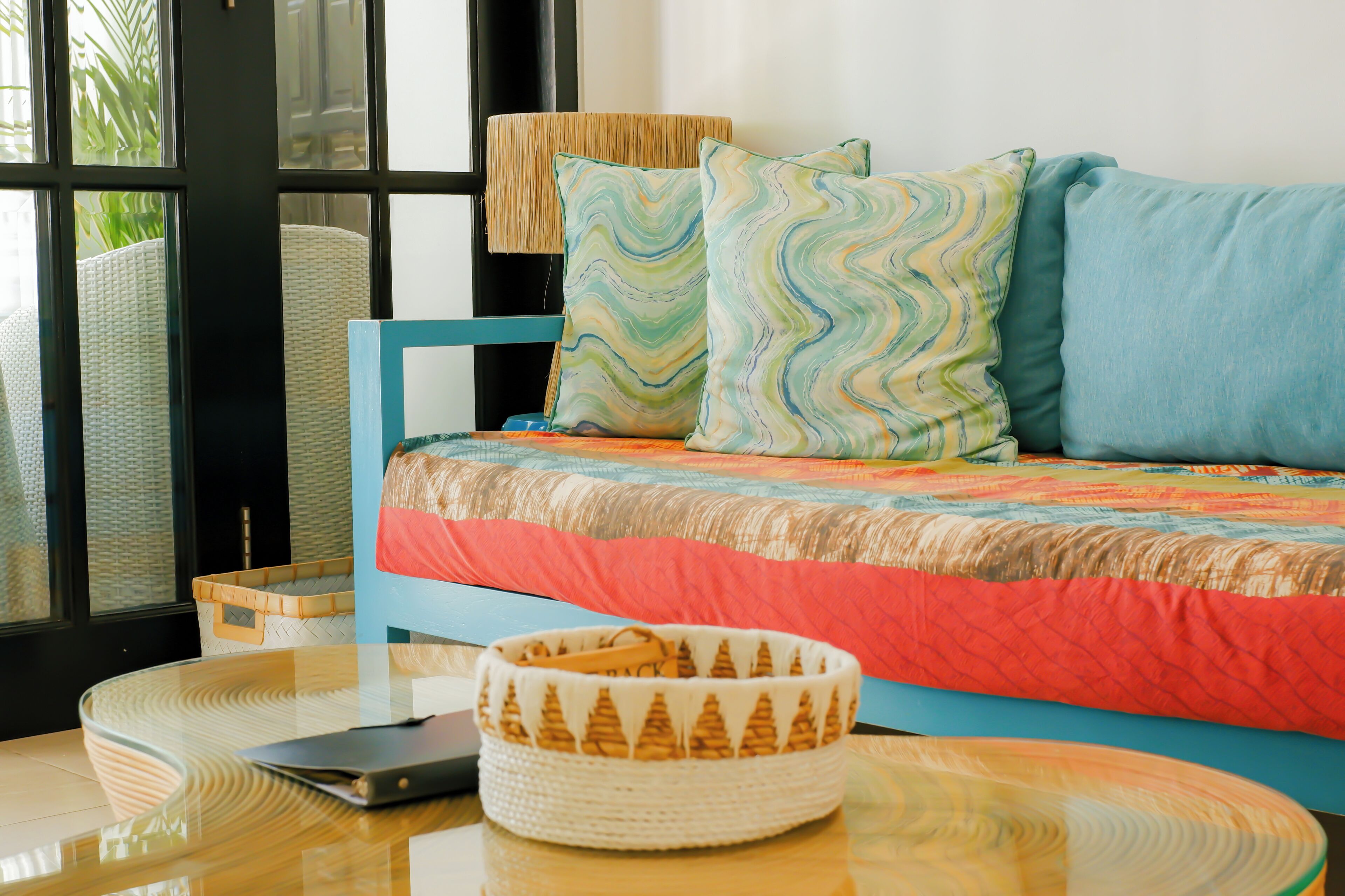 A bed with a blue headboard, a woven basket, and a smartphone on a glass table.
