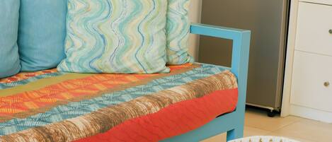 A bed with a blue frame, a patterned quilt, and two pillows. A microwave and refrigerator are visible in the background.