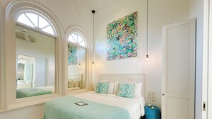A bedroom with a large bed, two windows, a mirror, and a colorful abstract painting. - Villa Neno (Seminyak)