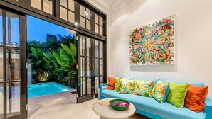 A modern living room with a pool, a blue sofa with colorful cushions, and a large abstract painting on the wall. - Villa Neno (Seminyak)