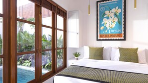 Un dormitorio con un ventanal grande, una cama con ropa de cama estampada y un cartel colgado en la pared.