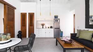 Una cocina moderna con armarios blancos, un microondas y un refrigerador. Hay un comedor con una mesa y sillas, y un sofá con cojines estampados.