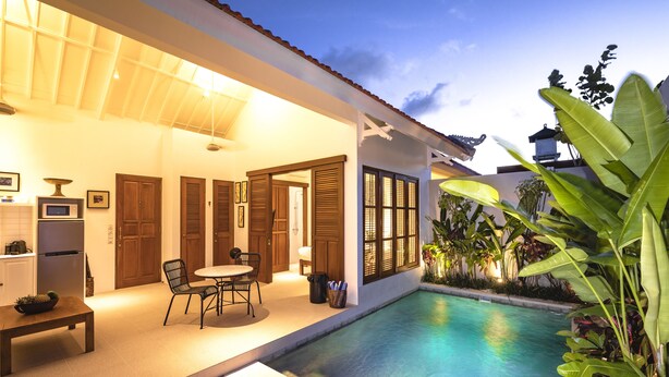A modern house with a swimming pool, a dining area, and a patio with chairs and a table. - Villa Pandi (Seminyak)