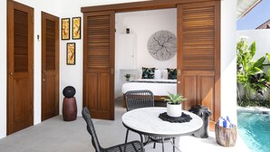 A modern room with a round marble table, black chairs, wooden doors, and a view of a swimming pool. - Villa Pandi (Seminyak)