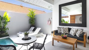 A modern outdoor living area with a pool, lounge chairs, a dining table, and a sofa with patterned cushions. - Villa Pandi (Seminyak)