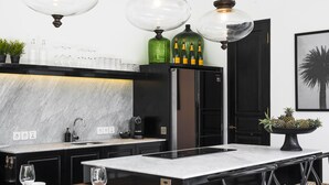 A modern kitchen with a marble countertop, black cabinets, and a central island with bar stools. - Villa Nago (Seminyak)