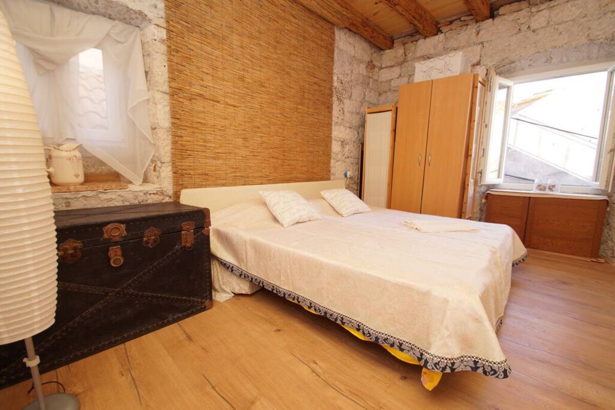 A bedroom with a bed, a wooden wardrobe, a suitcase, and a window.