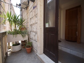A narrow alley with a stone wall, a wooden door, and potted plants.