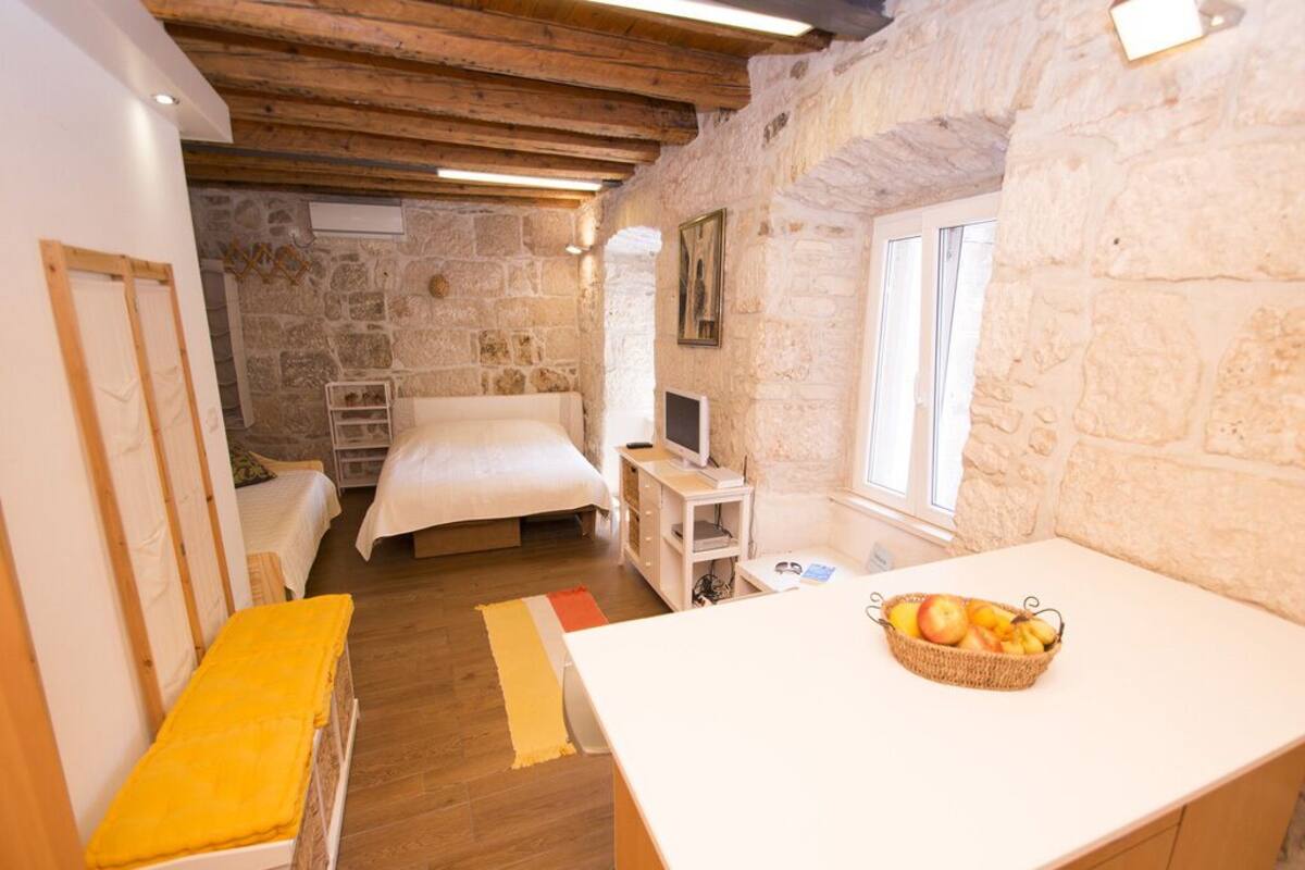 A cozy room with a bed, a desk with a computer, a stone wall, and a window.