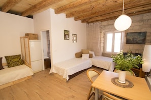 A cozy room with two beds, a wooden ceiling, a dining table with a vase, and a stone wall.