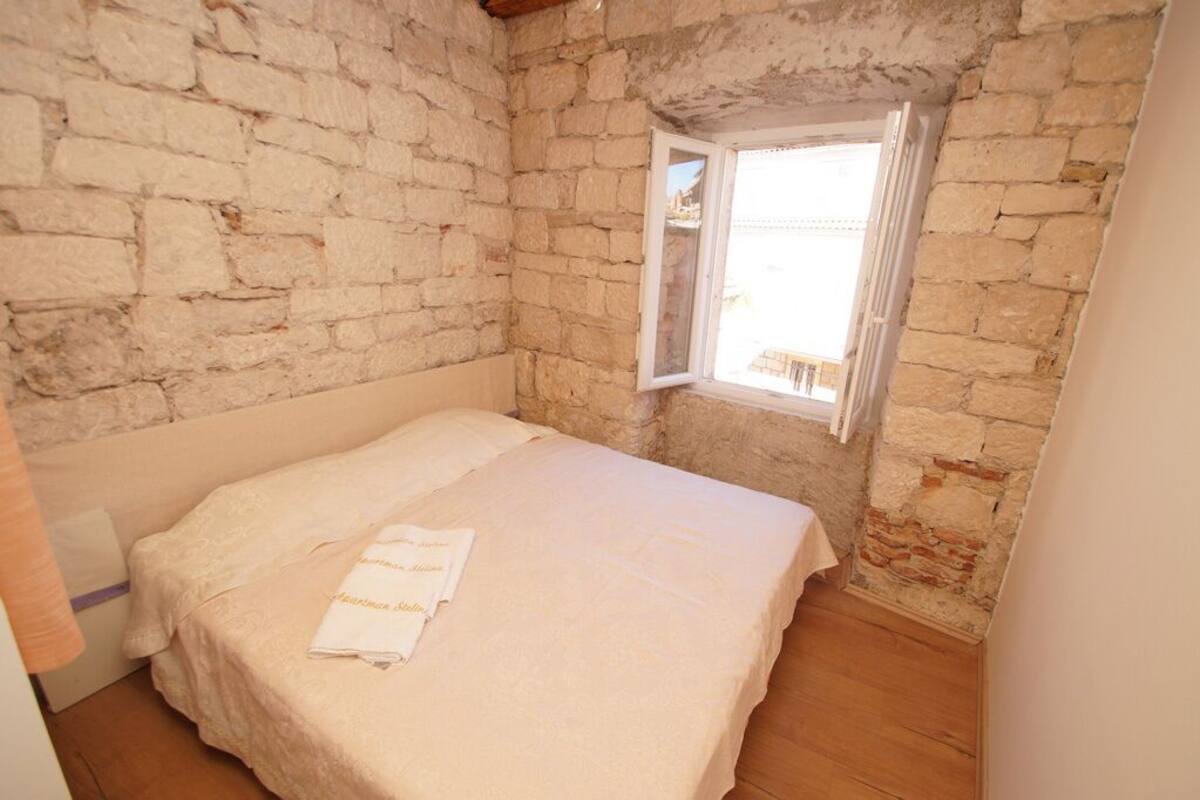 A small, stone-walled bedroom with a single bed, a window, and a wooden floor.