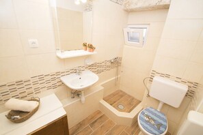 A bathroom with a sink, mirror, toilet, and shower area.