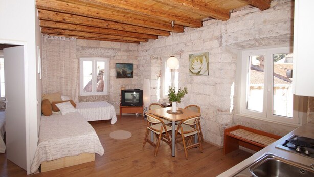 A cozy room with a bed, a TV, a dining table with chairs, and a kitchen area. - Apartments Stelina (Korcula)