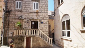 A stone building with a wooden staircase leading to a door, a small balcony, and a potted plant. - Apartments Stelina (Korcula)