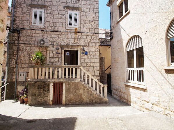 A stone building with a wooden staircase leading to a door, a small balcony, and a potted plant.