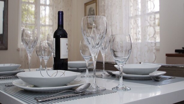A dining table set with white plates, clear wine glasses, and a bottle of wine. - Apartments Galerija (Korcula)