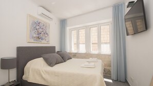 A bedroom with a bed, a TV mounted on the wall, and a window with curtains. - Apartments Galerija (Korcula)