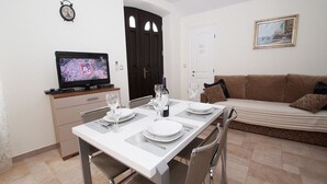 A dining area with a table set for two, a television on a stand, and a sofa in the background. - Apartments Galerija (Korcula)