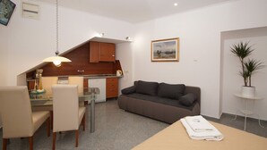 A compact living space with a kitchenette, a dining area, a sofa, and a small table with a towel. - Apartments Galerija (Korcula)