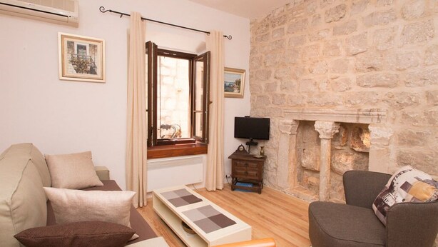 Un salon avec un mur en pierre, une cheminée, un téléviseur et une fenêtre avec des rideaux.