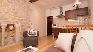Un salon chaleureux avec un mur en pierre, une cheminée, un canapé et un coin repas doté de meubles en bois et d’un four à micro-ondes.