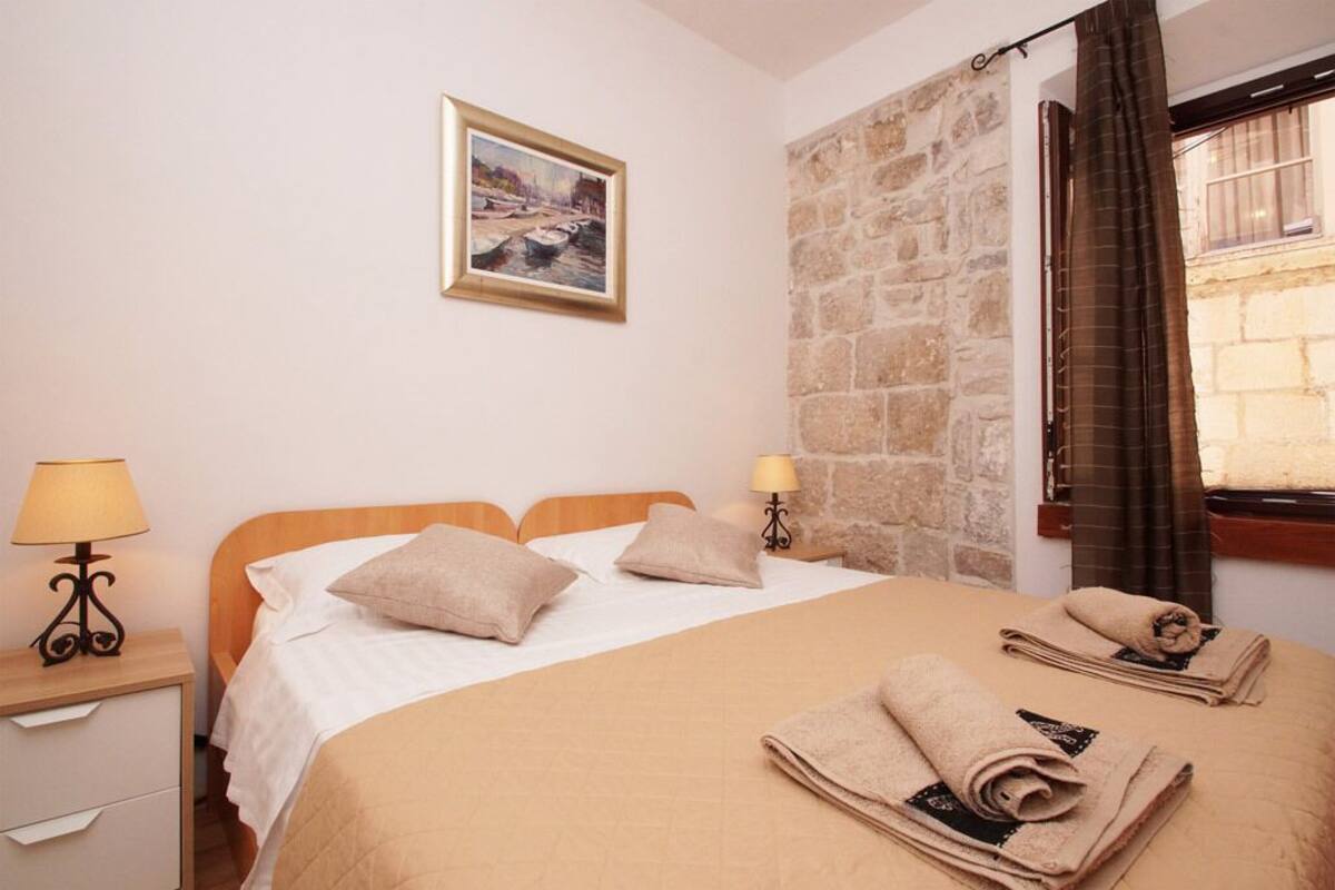 Quarto de hotel com cama, duas luminárias de cabeceira, um quadro na parede e janela com cortinas.