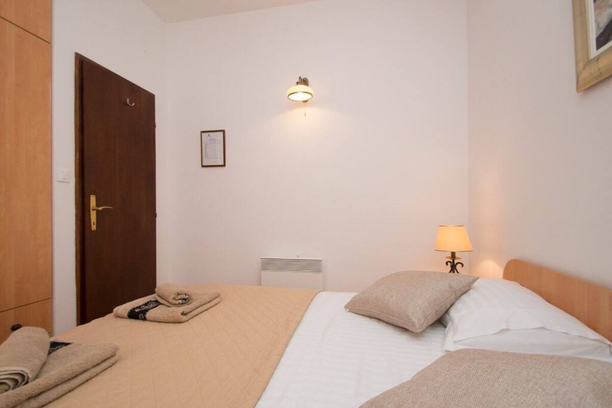 Quarto de hotel com uma cama, luminária de cabeceira, radiador e porta.