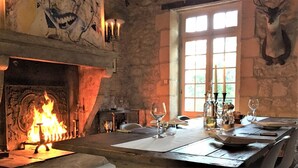 Uma sala de jantar com lareira, paredes de pedra e uma mesa posta para refeição.