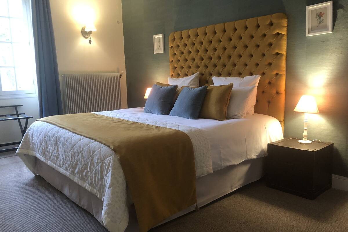 Een net opgemaakt bed met een gestuufd hoofdbord, een bedlampje en een ingelijste foto aan de muur.