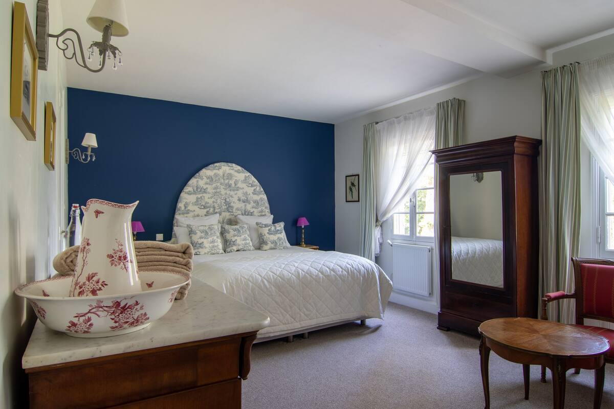 Een slaapkamer met een groot bed, een dressoir, een spiegel en een stoel.
