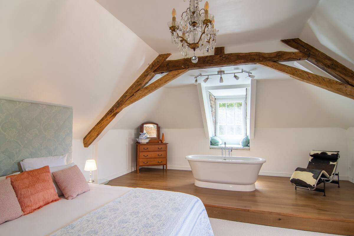 Een slaapkamer met een groot bed, een kaptafel met spiegel, een badkuip en een raam met uitzicht.