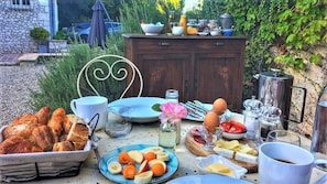 Disposição de pequeno-almoço ao ar livre com pão, frutas, ovos e bebidas sobre uma mesa.