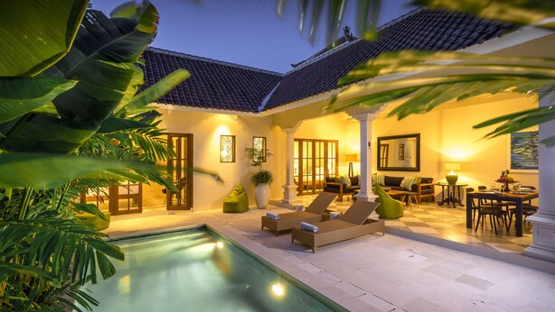 Un espacio exterior bien iluminado con piscina, sillas de descanso y una mesa de comedor para dos.
