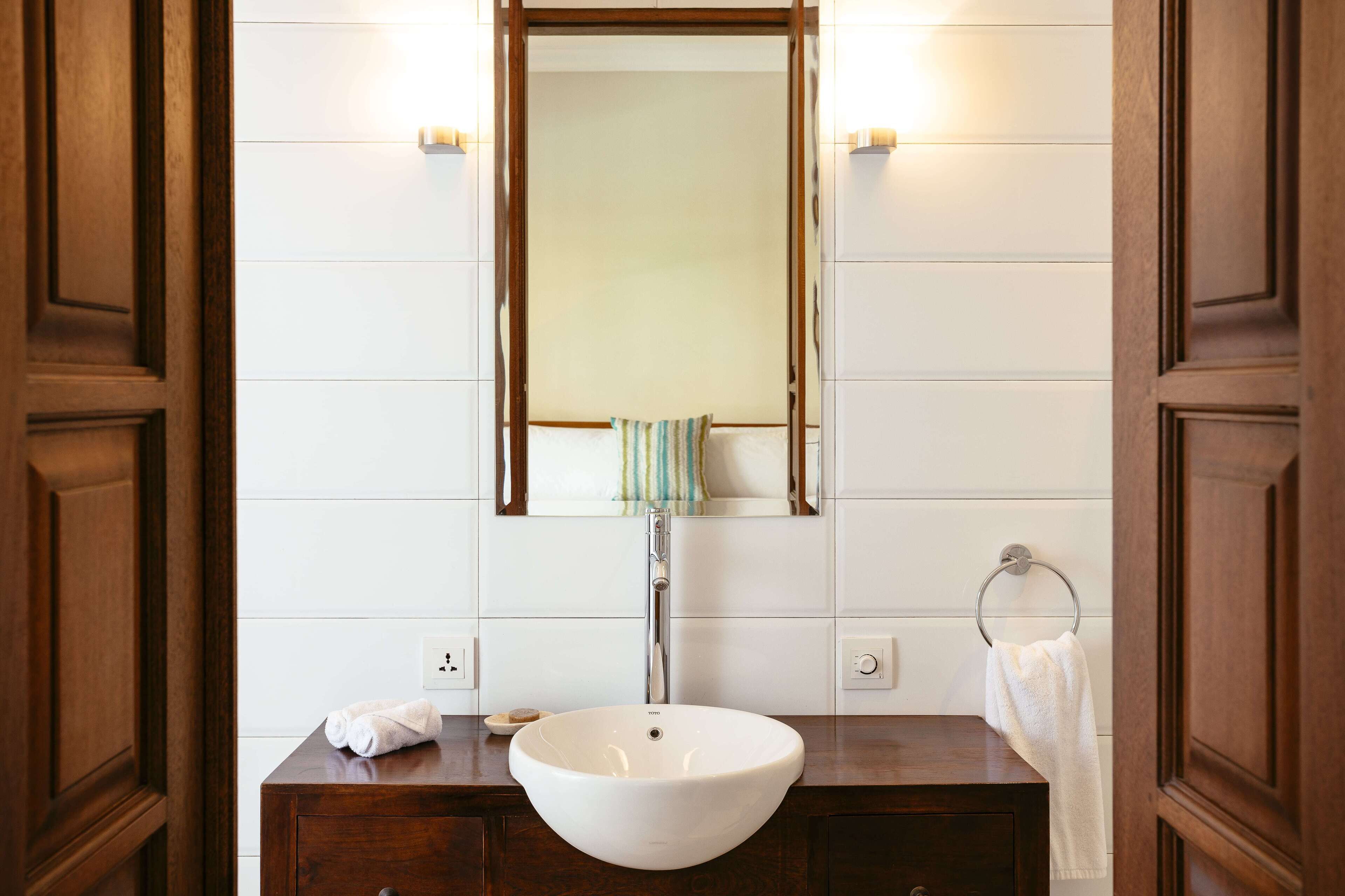 A bathroom with a wooden vanity, a white sink, a mirror, and a towel rack.