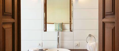 A bathroom with a wooden vanity, a white sink, a mirror, and a towel rack.