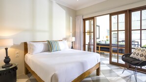 Habitación de hotel con una cama grande, una mesita de noche con lámpara, una silla y vistas al área de estar exterior a través de una puerta de cristal.