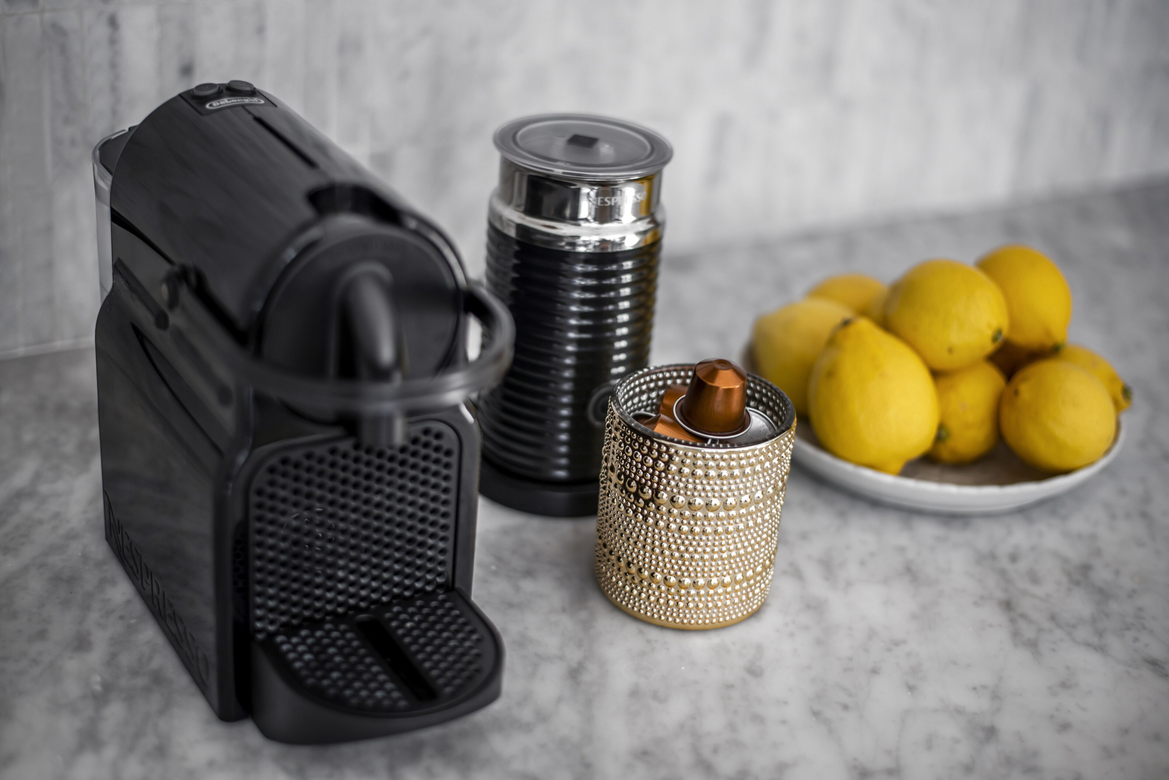 Et køkken med kaffemaskine, en metalbeholder og en tallerken med citroner.