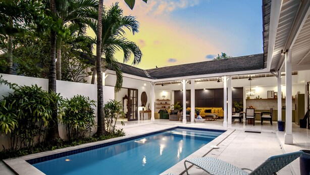 A swimming pool with lounge chairs, surrounded by greenery and a covered patio area. - Beachhouse (Canggu)