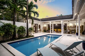 A swimming pool with lounge chairs, surrounded by greenery and a covered patio area. - Beachhouse (Canggu)