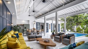 A spacious living area with a pool, yellow and green sofas, and a wooden coffee table. - Beachhouse (Canggu)