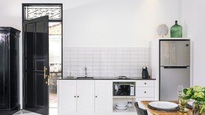 A modern kitchen with white cabinets, a black door, and a dining area with a wooden table and chairs. - Town House (Canggu)