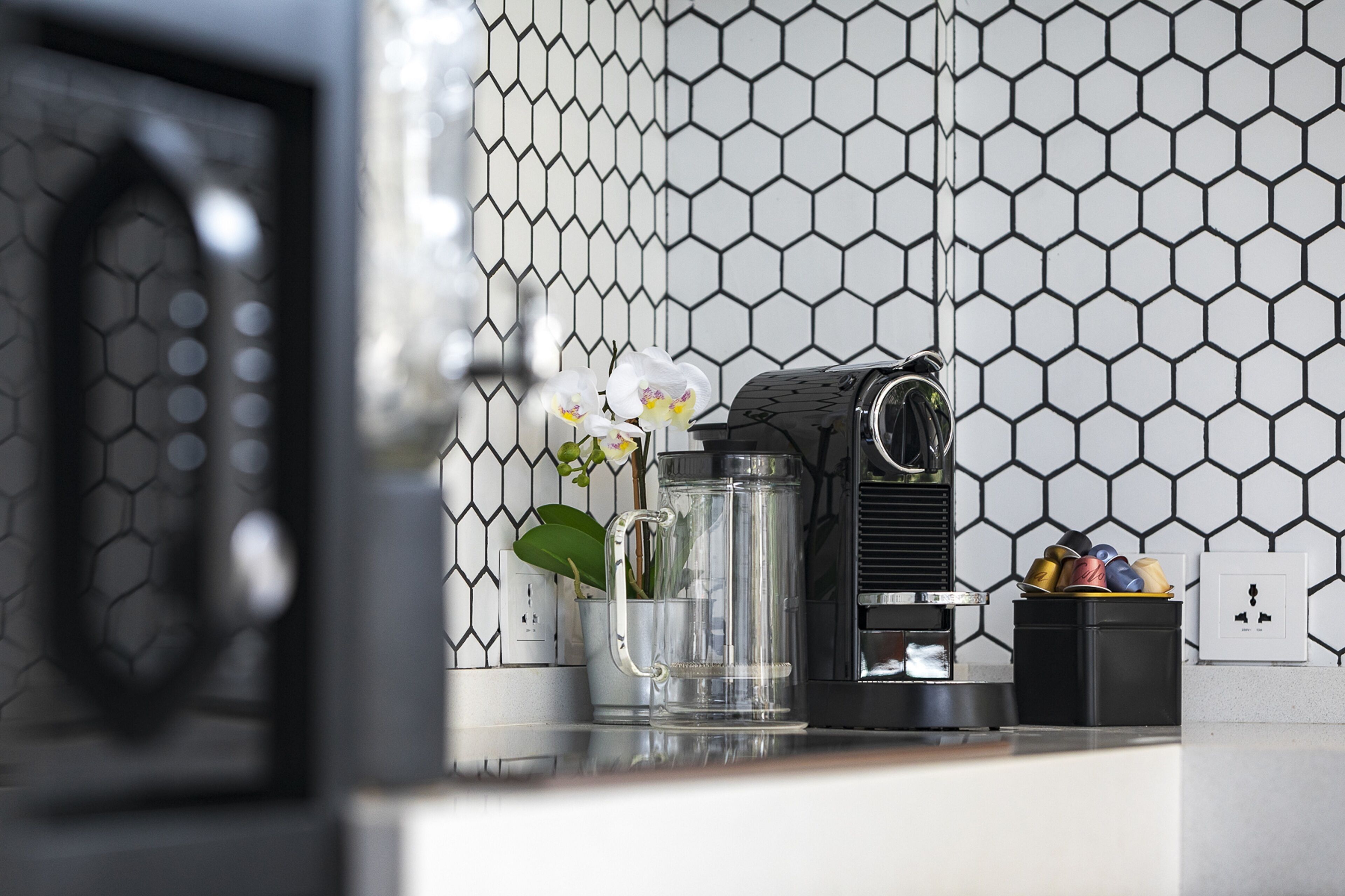 Una encimera de cocina con una cafetera, una taza de vidrio y una orquídea en maceta.