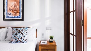 A neatly made bed with patterned pillows, a framed Indonesian stamp, a small potted plant, and a wooden nightstand with a magazine. - Villa Salsa (Seminyak)