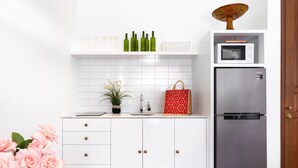 A kitchen with white cabinets, a stainless steel refrigerator, a microwave, and a shelf with green bottles and glasses. - Villa Salsa (Seminyak)