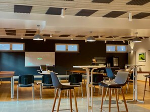 Et moderne mødelokale med projektorskærm, borde, stole og kaffestation.