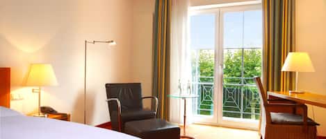 A hotel room with a bed, a desk, a chair, a phone, and a balcony with curtains.