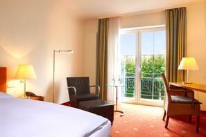Una camera d'albergo con un letto, una scrivania, una sedia, un telefono e un balcone con tende.