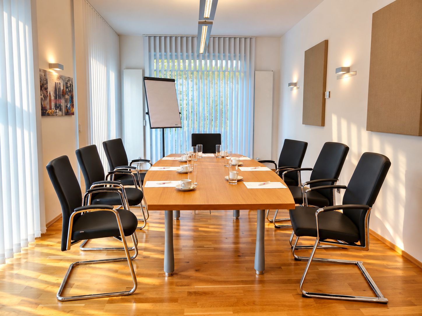 Ein Konferenzraum mit einem langen Tisch, schwarzen Stühlen und einer Whiteboard-Wand.