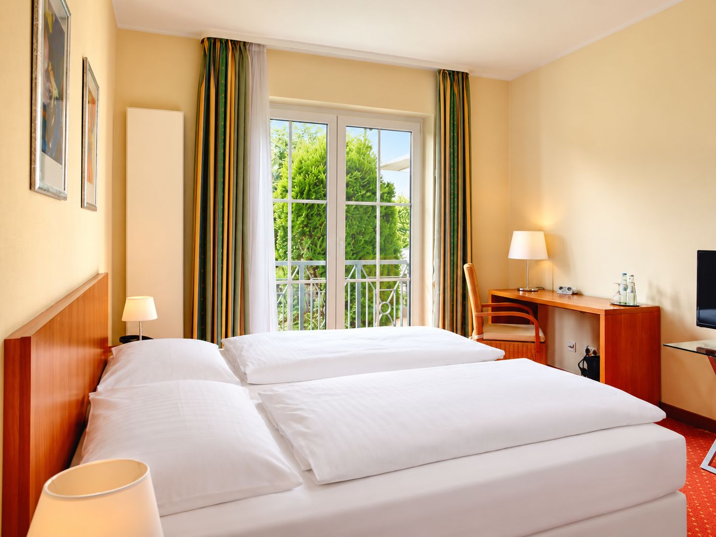 Habitación de hotel con cama doble, un escritorio con silla, televisión y ventana con cortinas.