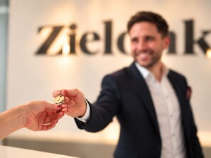 A person handing over a key to another person in a business suit with a sign in the background. - Hotel Zielonka (Hochheim am Main)